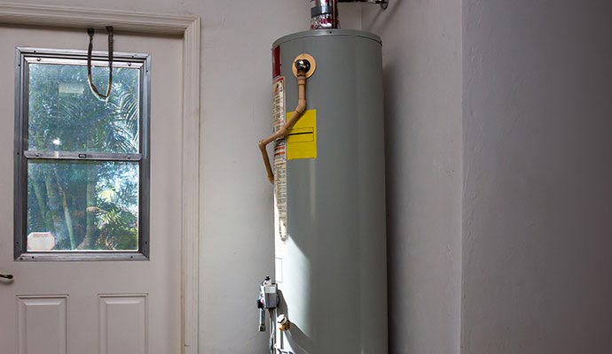 A vertical hot water heater tank standing in the corner of a room