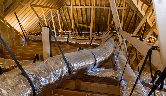Extensive network of silver insulated flexible ducts supported by black straps in a wood-framed attic space