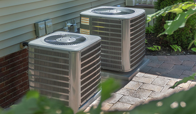 Two grey outdoor AC condenser units installed on concrete pads