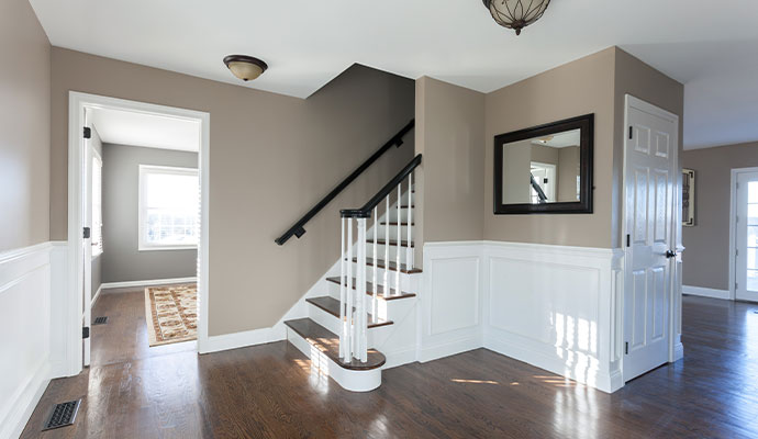 A clean home interior featuring a wooden staircase and hallway with black metal floor registers installed for a forced air heating and cooling system