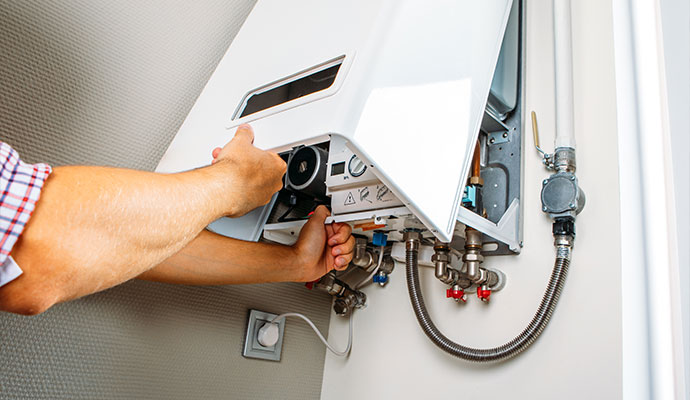 A technician removing the white protective front casing of a wall-mounted gas boiler