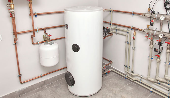 A tan residential indoor furnace unit with white PVC drainage pipes