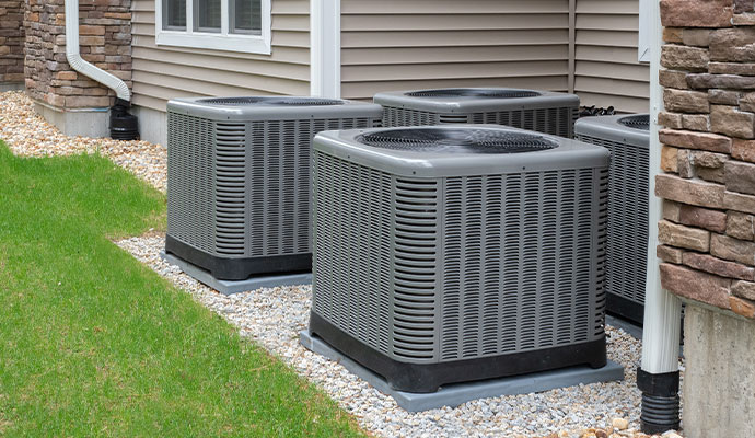 Four grey vertical air conditioning condenser units installed in a row on concrete pads