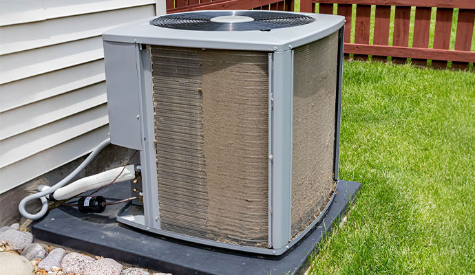 An outdoor air conditioner unit showing heavy dirt and dust buildup on its metal condenser coils