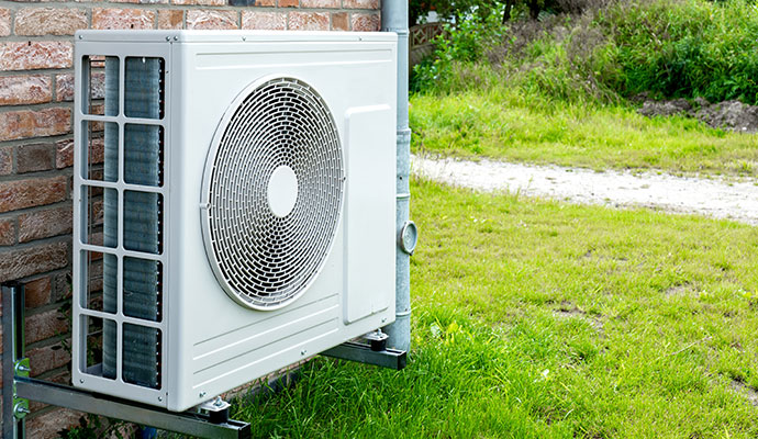 White slim-profile air conditioning condenser mounted on metal wall brackets against a brick wall
