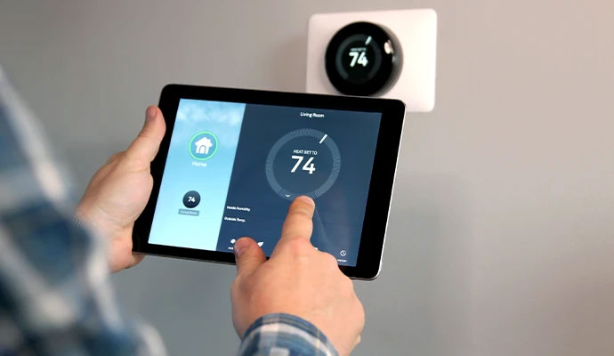 Person adjusting home temperature on tablet with smart thermostat mounted on wall