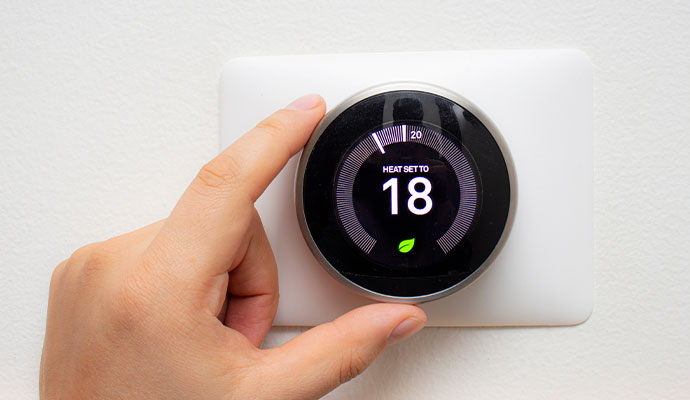 A close-up of a hand turning the dial on a modern round smart thermostat mounted on a white wall