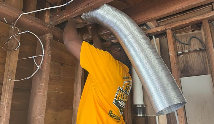 Technician installing a flexible silver vent duct in a wooden ceiling frame