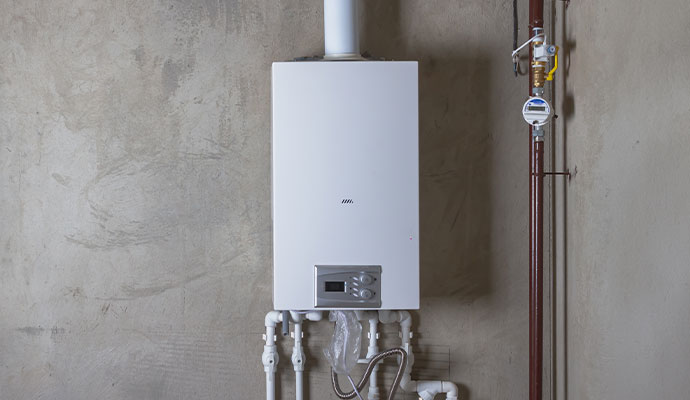 White rectangular gas boiler mounted on a concrete wall with white piping and a gas meter nearby