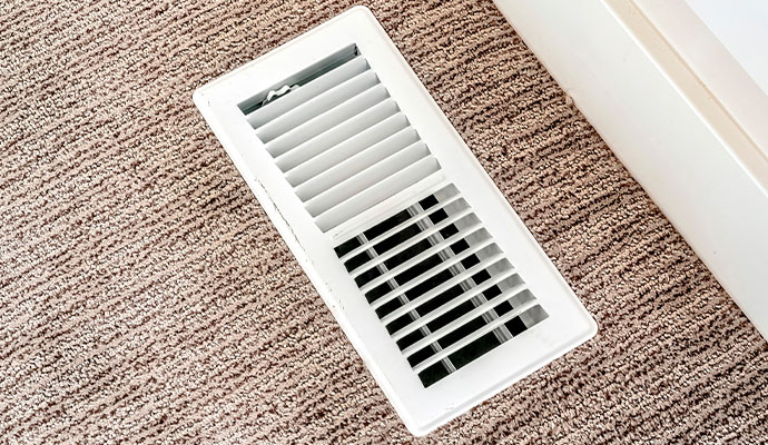 A white rectangular metal floor register installed in a room